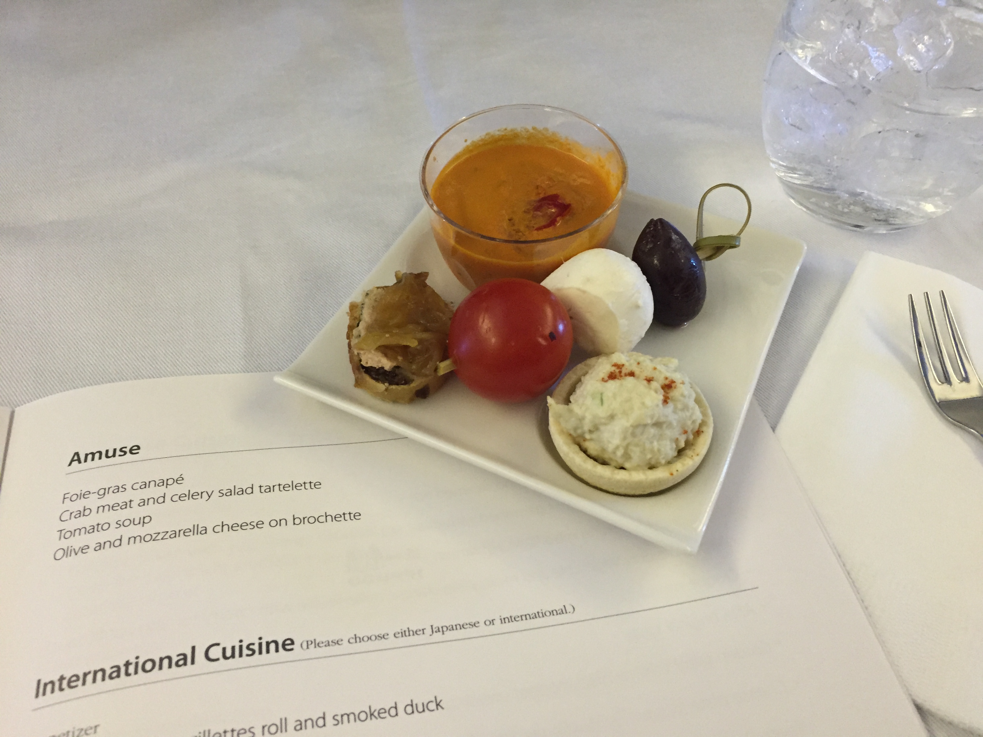 Amuse plate — foie gras canapé, tomato soup shot, crab tartelette, mozzarella ball, olive