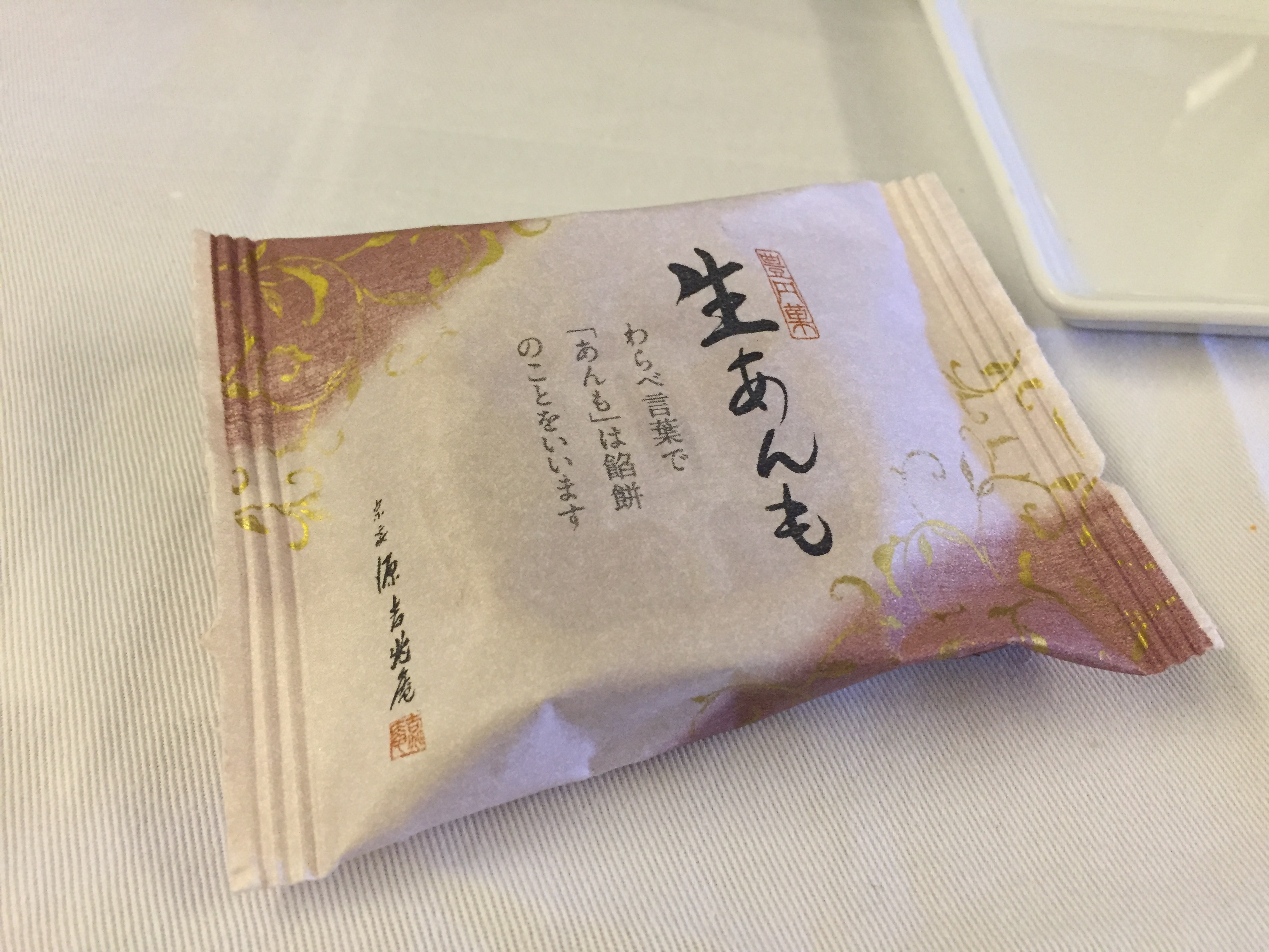 A wrapped Japanese sweet — gold and pink wrapper with calligraphy, "NAMAANMO" red bean mochi