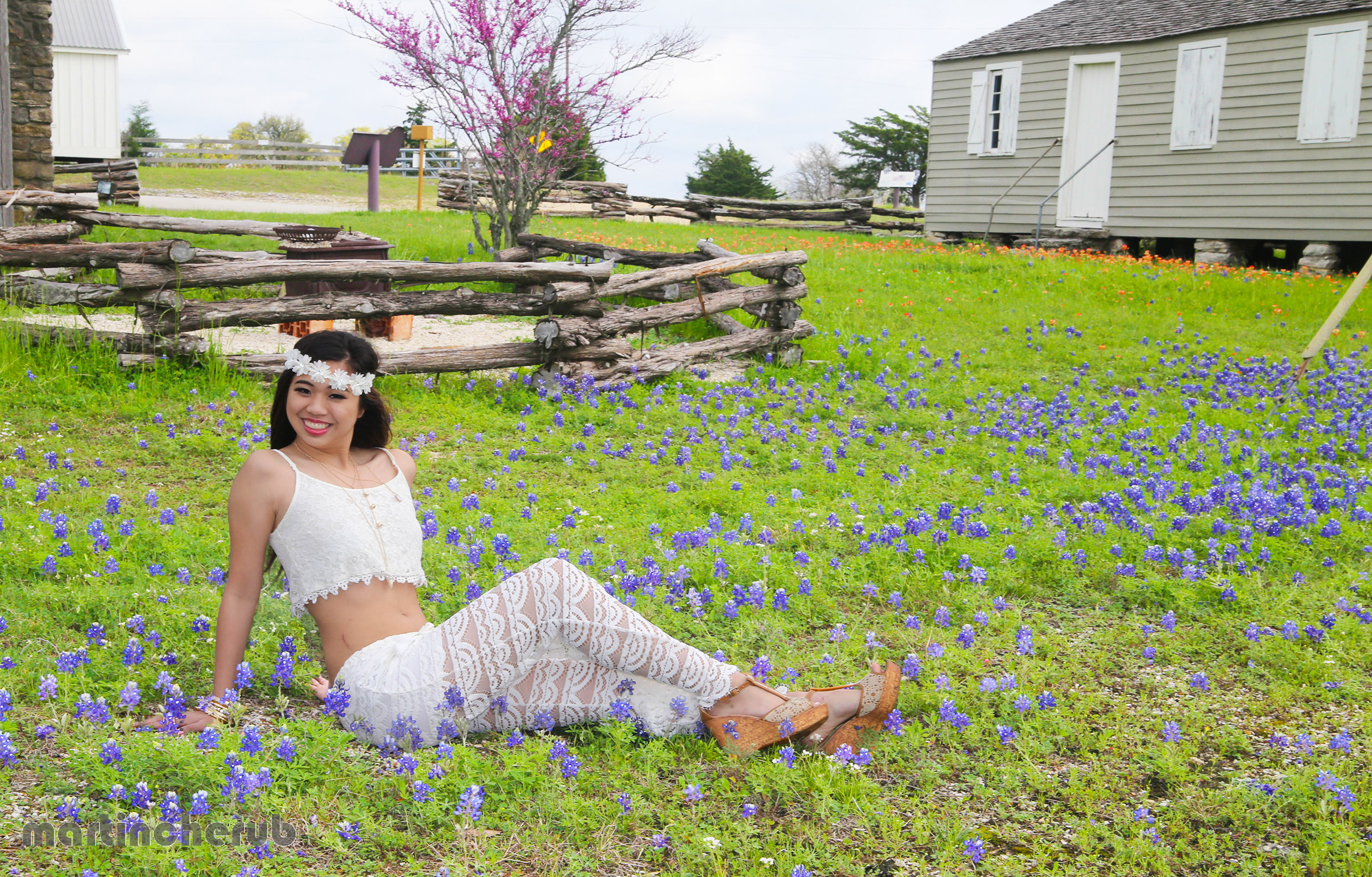 Tiffany Dimaano sitting in a carpet of bluebonnets near a historic farmhouse in Brenham, Texas