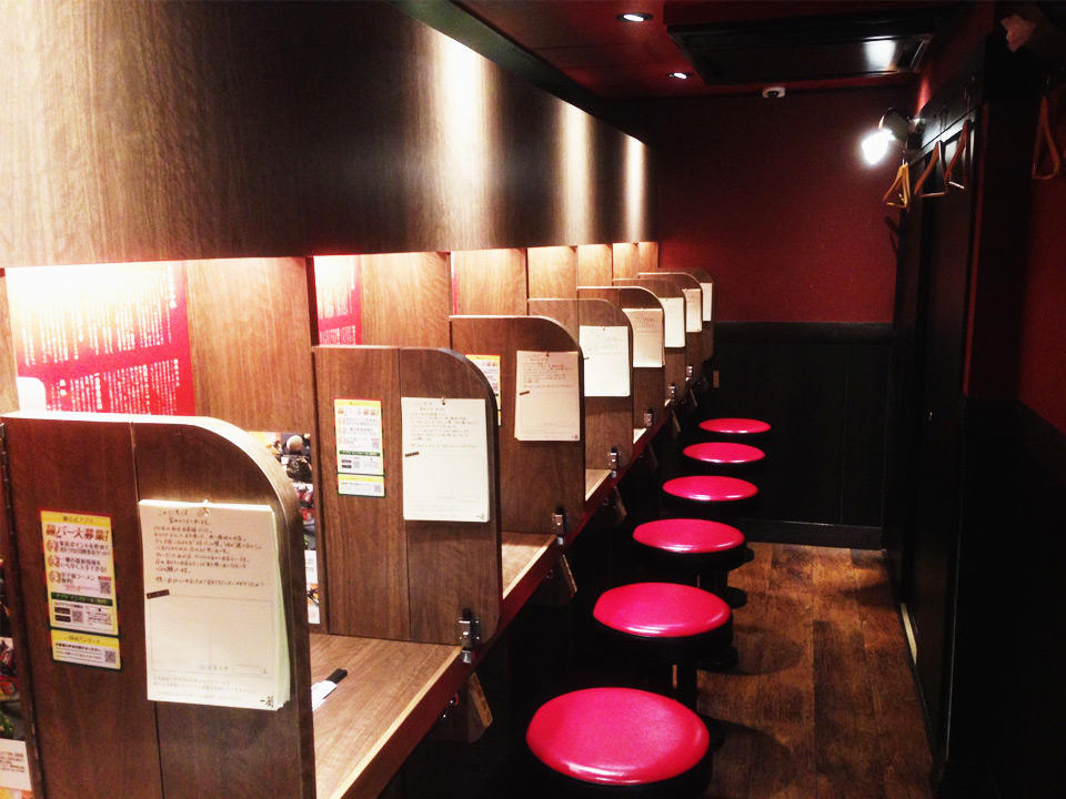 Row of individual dining booths with wooden partitions and red stools