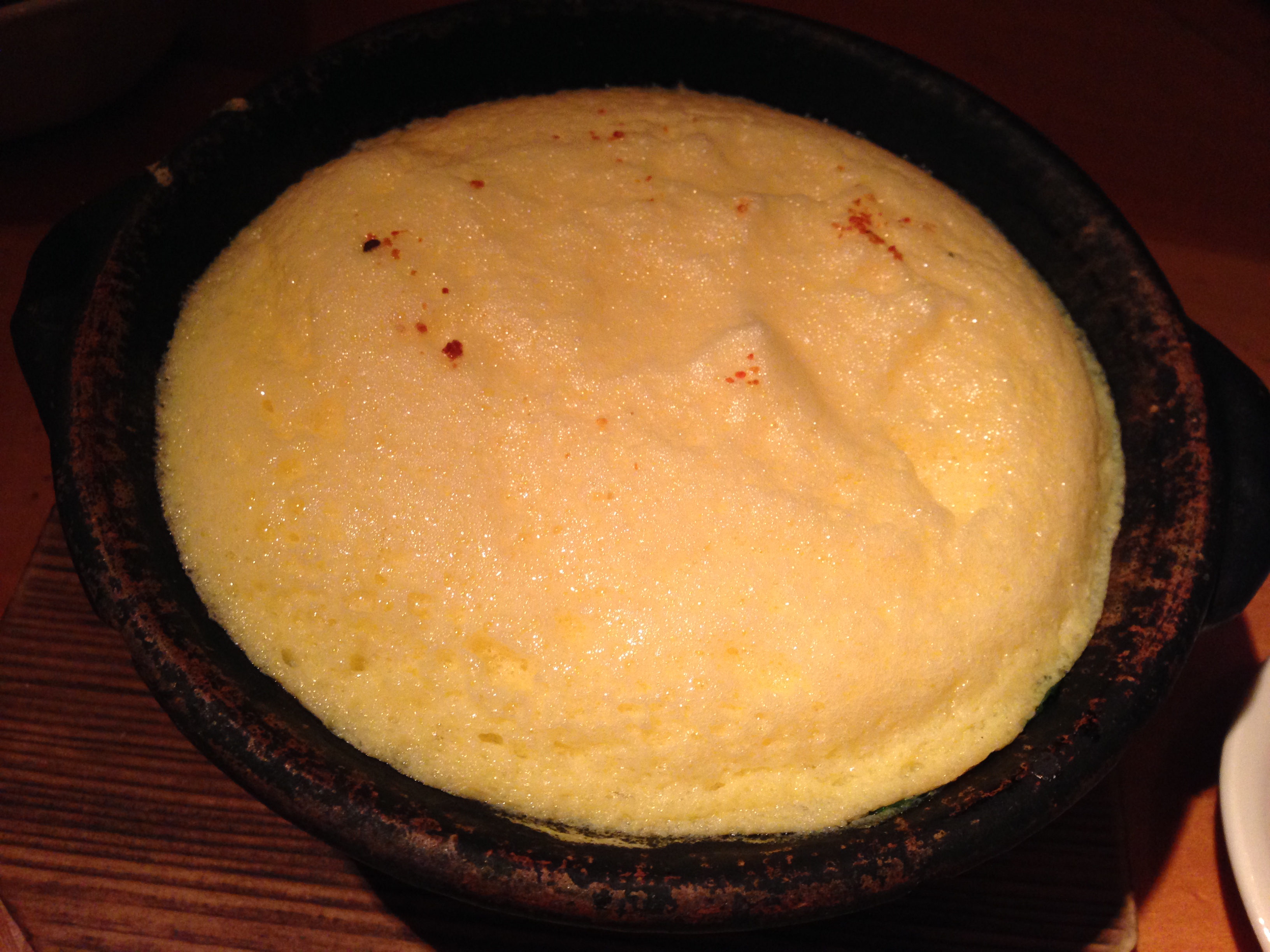 A puffy soufflé-style omelette covering congee in a cast iron pan