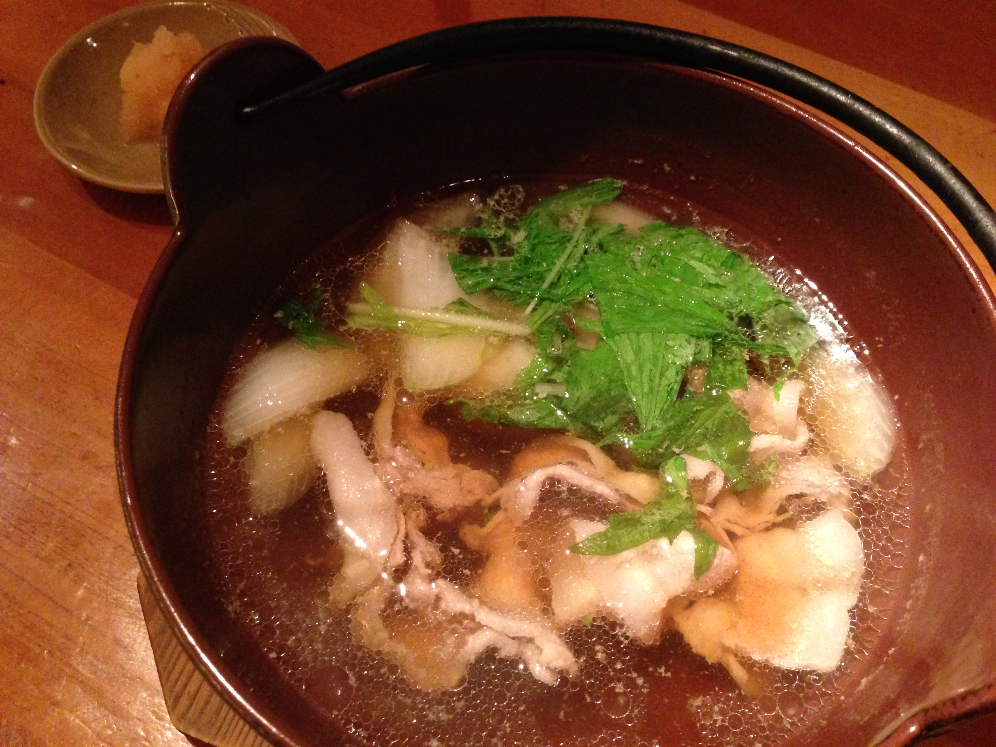 A clear soup with thinly sliced pork, onion, and shiso leaves