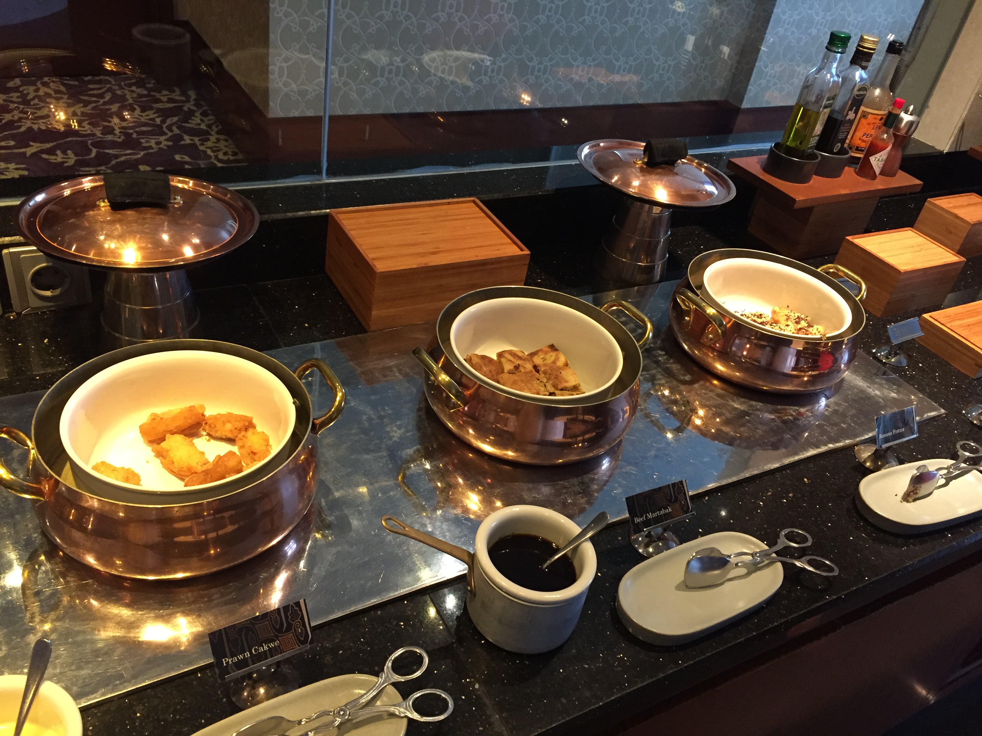 Copper-coloured chafing dishes filled with prawn cake, beef rendang, and assorted hot dishes