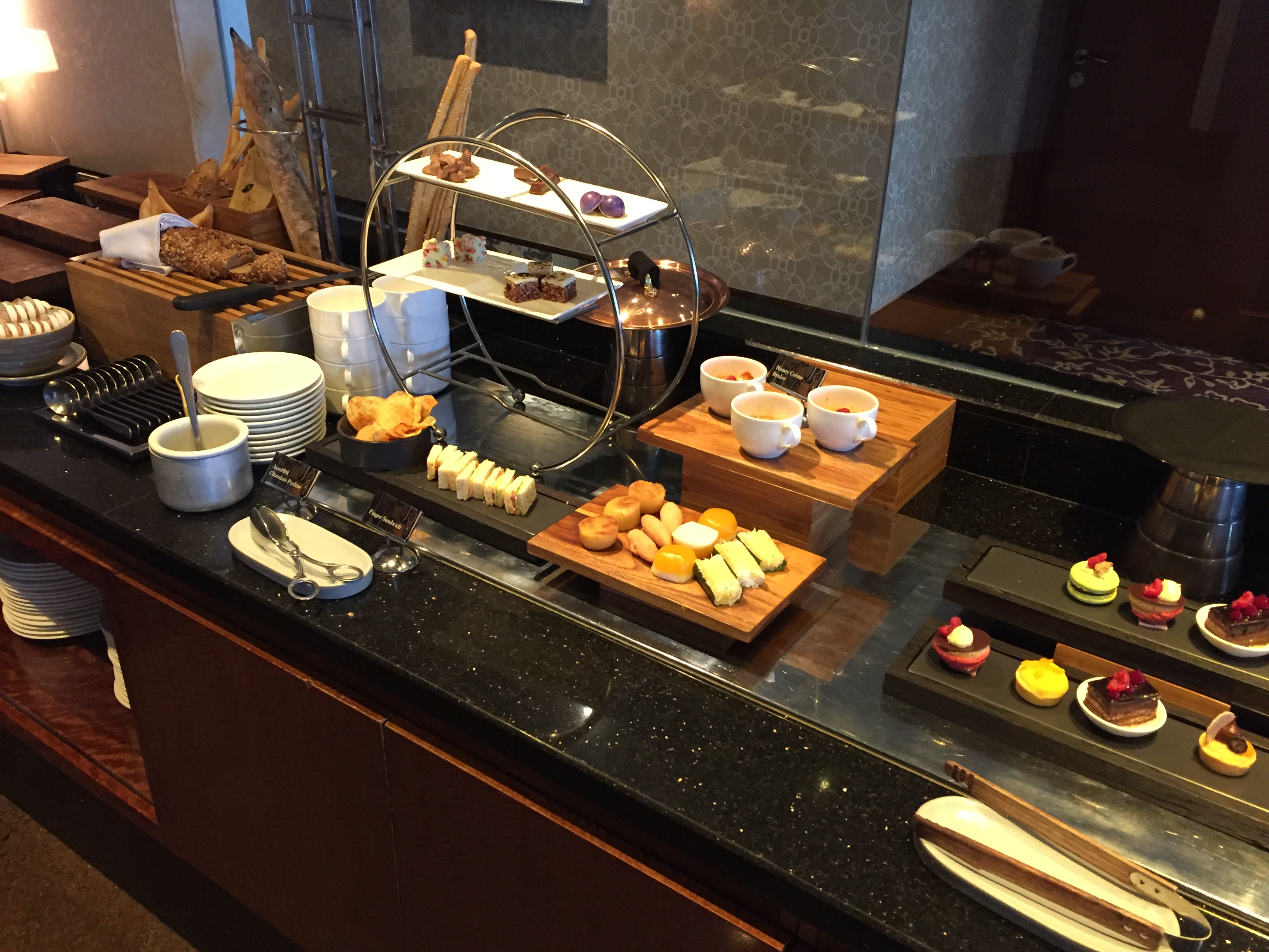 Afternoon tea spread — sweets on a tiered stand, scones, finger sandwiches, individual desserts on slate platters