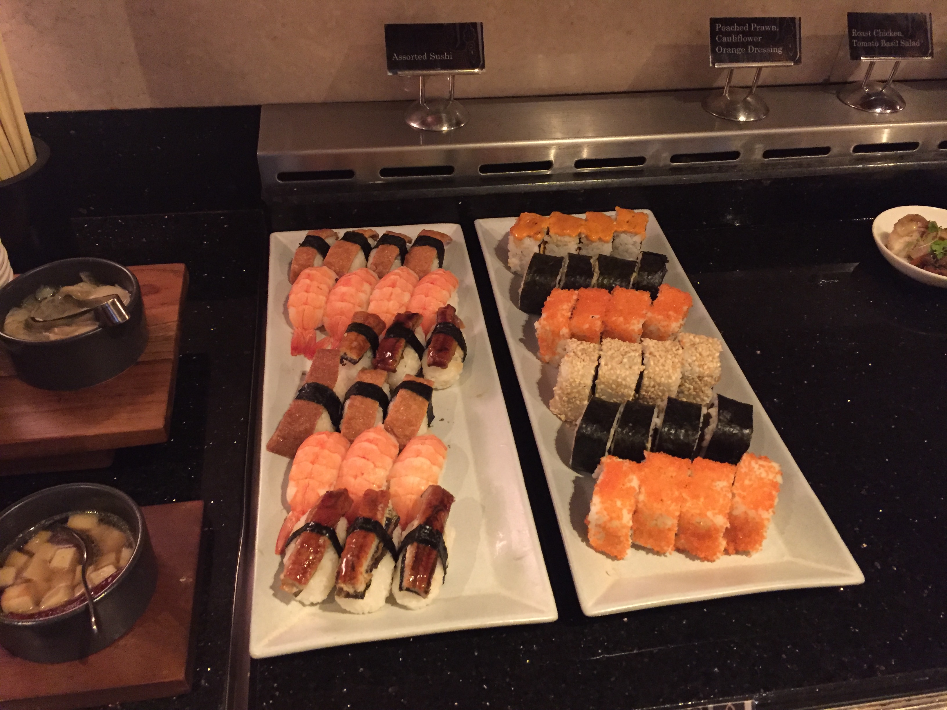 Two long platters of assorted sushi — salmon, tuna, and unagi nigiri alongside maki rolls and tobiko-coated rolls, served at the lounge with miso soup on the side