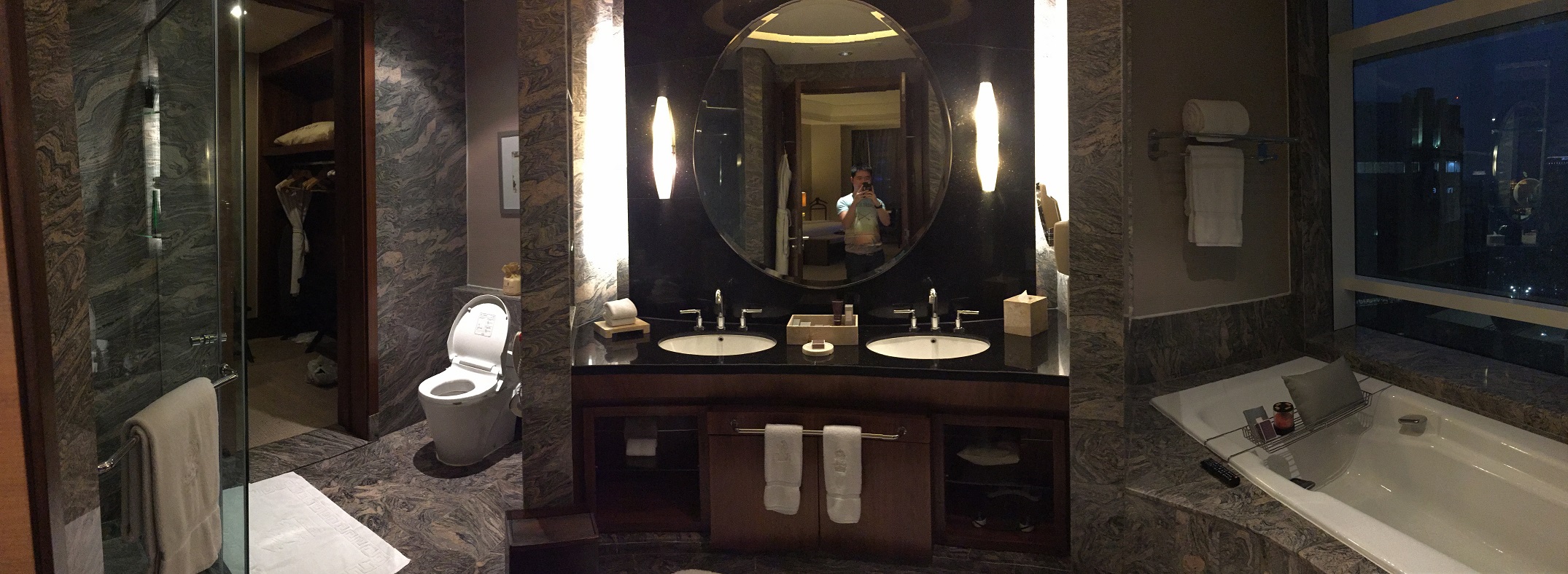 Marble-clad bathroom panorama — deep soaking tub, glass shower stall, double vanity, enclosed water closet, and floor-to-ceiling window