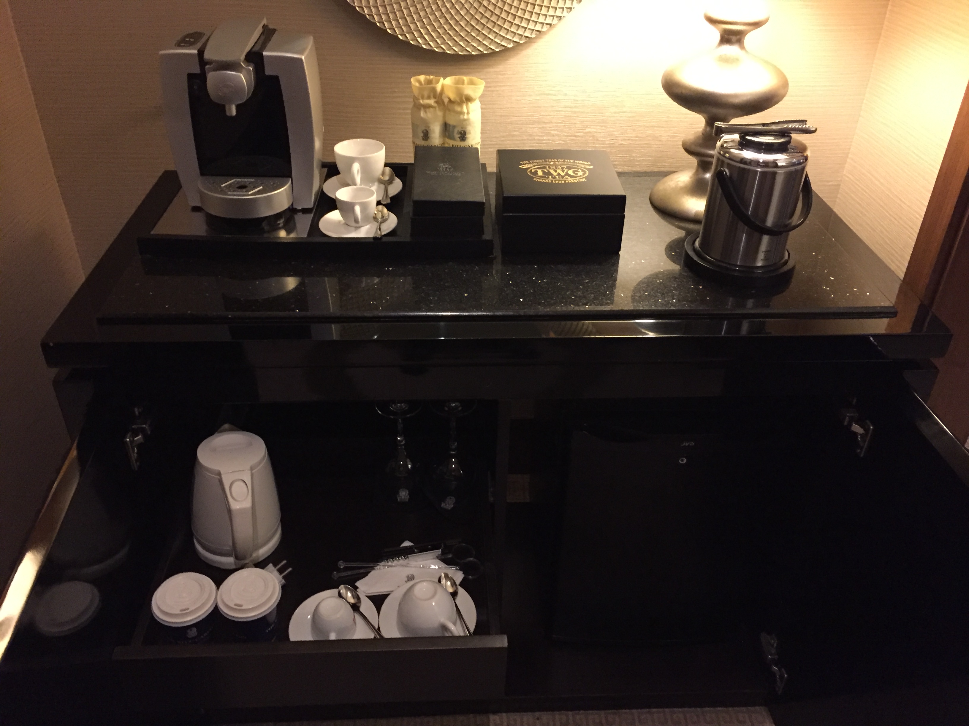 A coffee and tea station — Nespresso machine, twin demitasse cups, a TWG tea presentation box, and a stainless-steel ice bucket on a black-stone counter