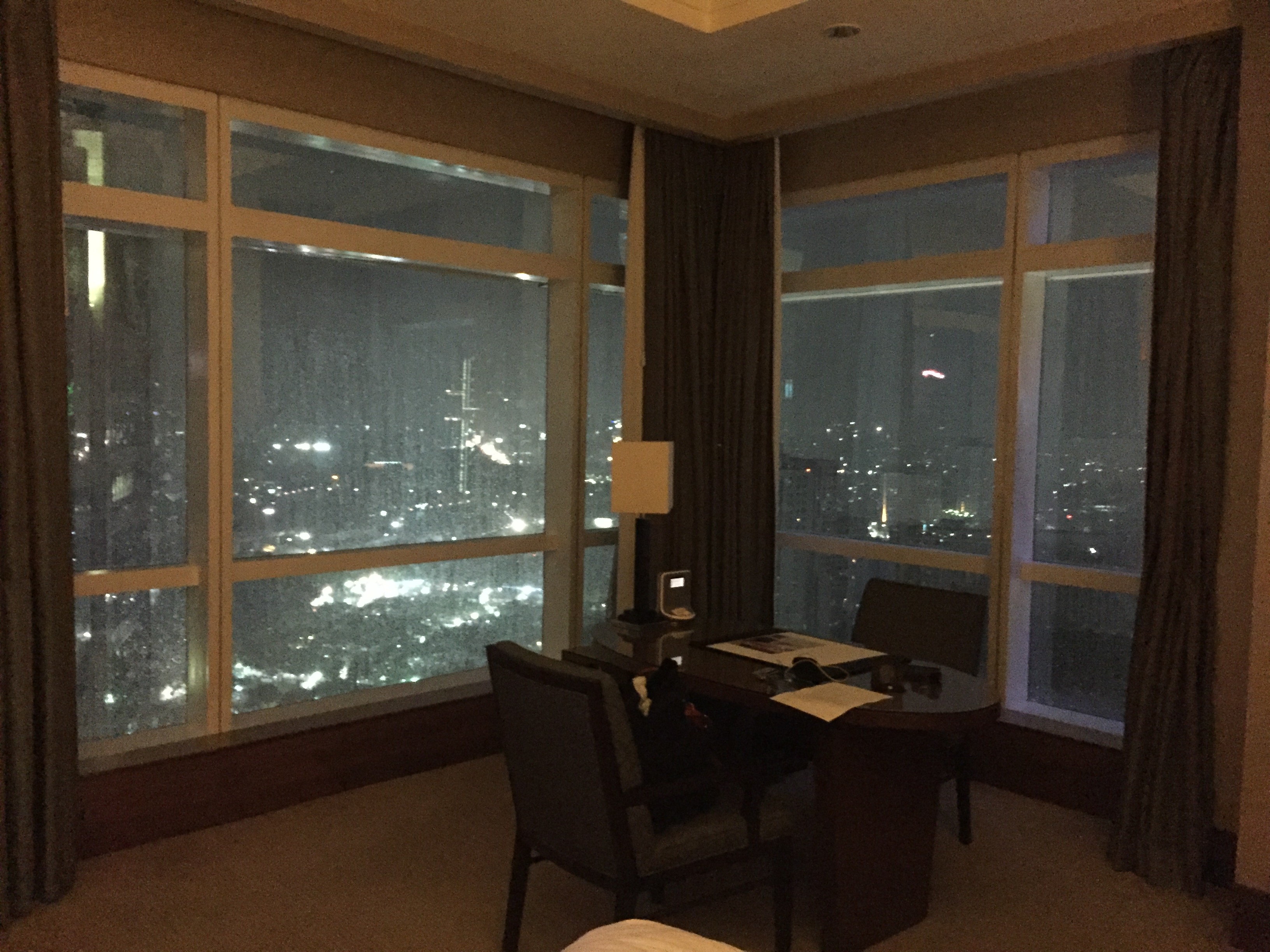 The corner desk at night, with floor-to-ceiling windows on two sides showing Jakarta's skyline lit up against the dark sky