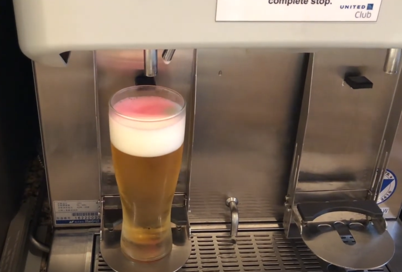 A self-pour Asahi beer dispenser at the United Club — a glass of cold beer with foamy head being filled at the press of a button