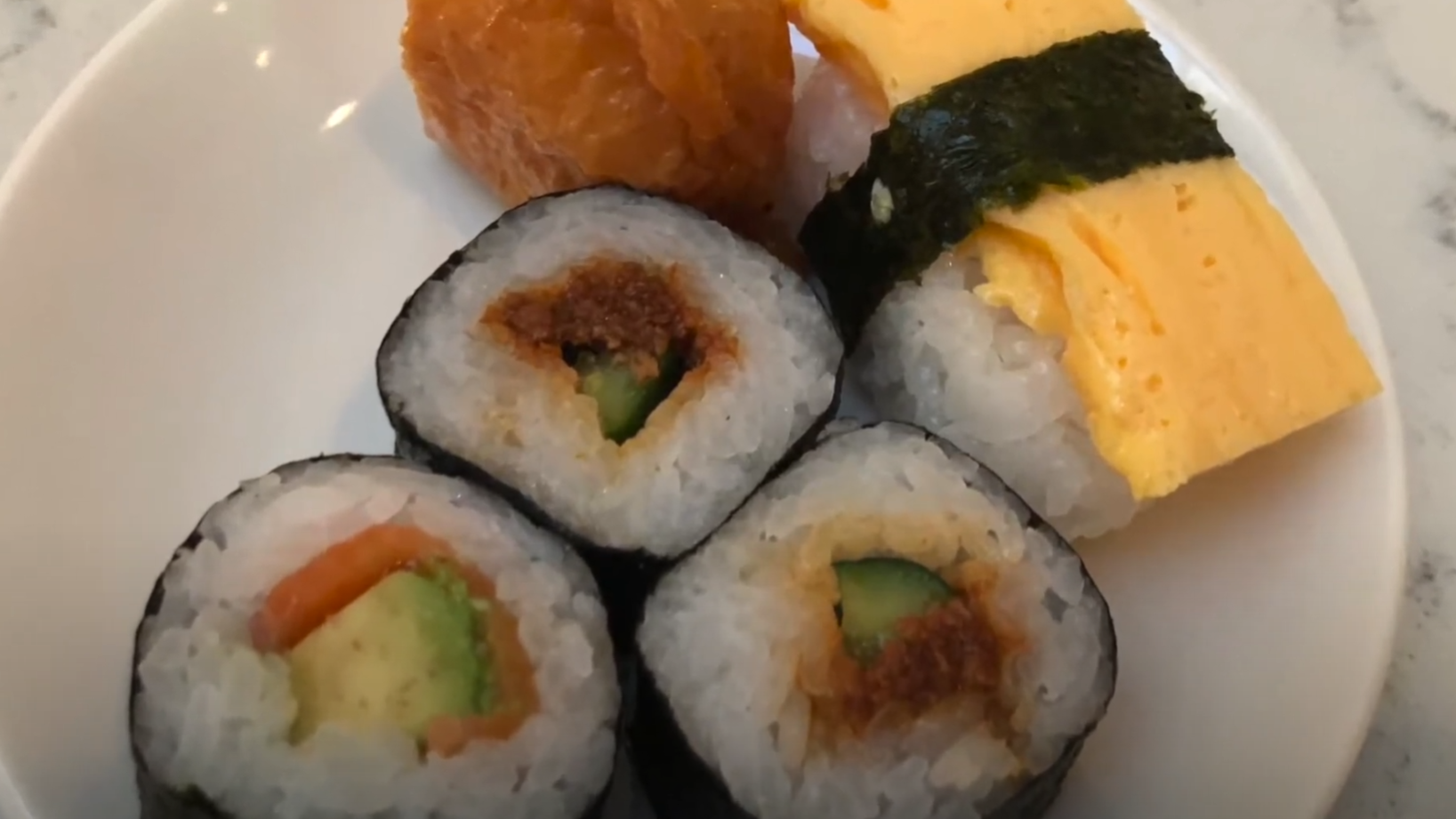 A small plate from the United Club lounge — assorted sushi maki, an inari tofu pouch, and tamagoyaki egg slices wrapped in nori